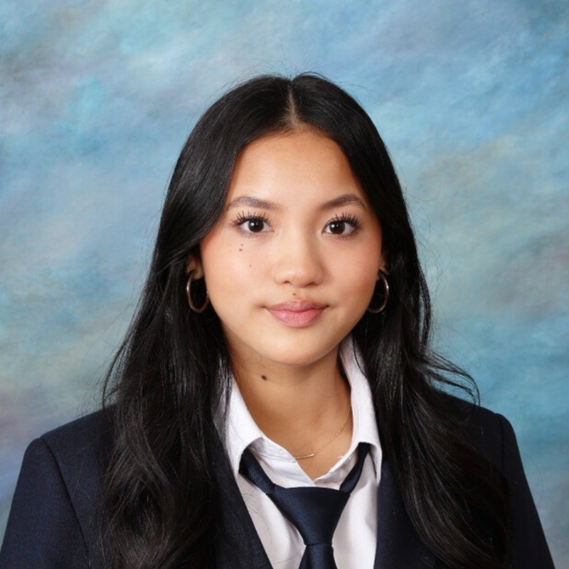 Leah Tran — professional headshot in navy blazer, white shirt, and tie; square studio portrait.
